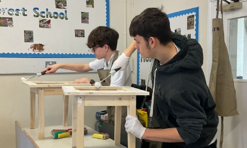 Two construction students working side by side painting their side tables with a roller brush